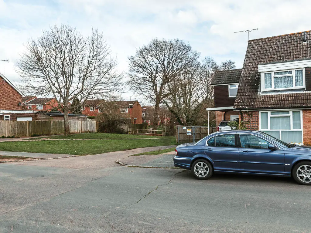 Looking across a residential road to a green past the hoses. There is a blue parked car in front of one of the houses.