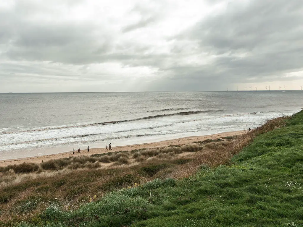 Looking down the green to the beach and sea below. There are people walking on the beach.