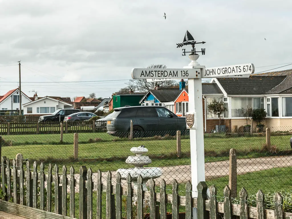 A white sign in someone's front garden pointing the way to Amsterdam and John O'Groats.