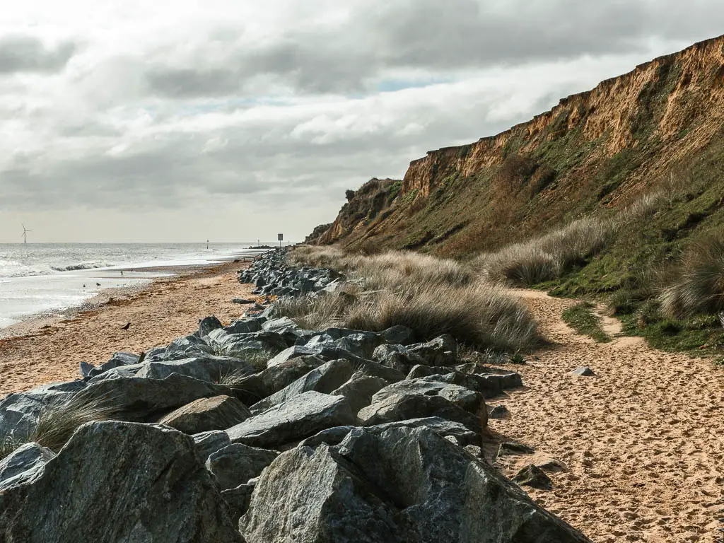 Looking straight along the sand beach with a strip of large rocks running through it, and the cliffs to the right on the walk between Hemsby and Great Yarmouth.