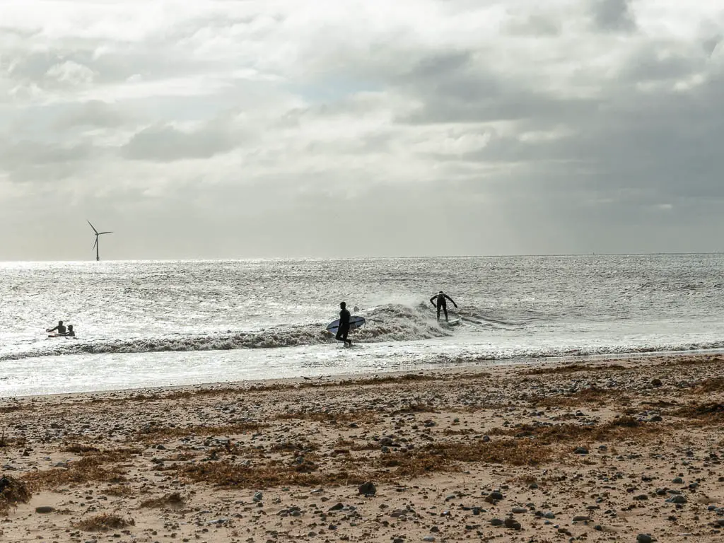 Looking across the sandy beach to surfers on the sea on the walk from Hemsby to Great Yarmouth.