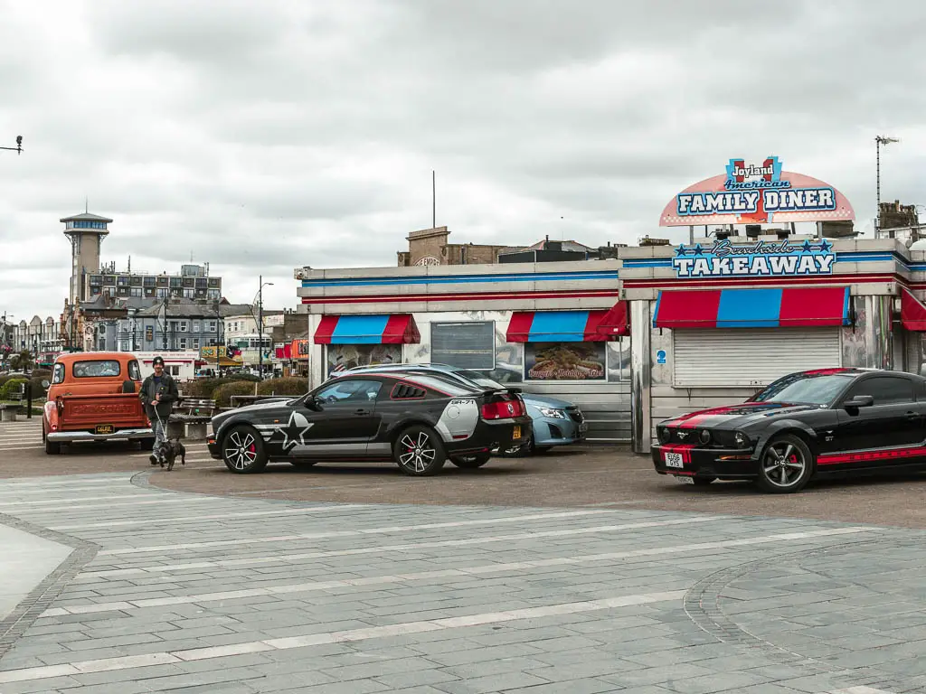 A closed diner with red and blue canopies, and retro cars parked outside in Great Yarmouth. 