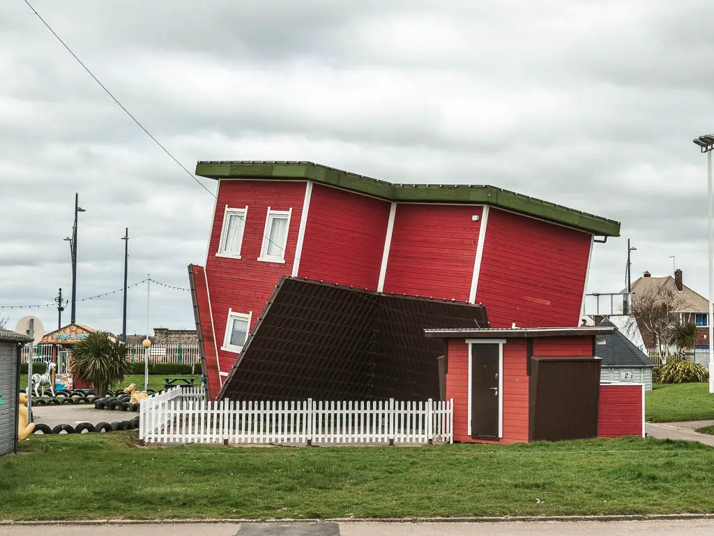 An upside down red house on the green with a white picket fence around it, in Great Yarmouth.