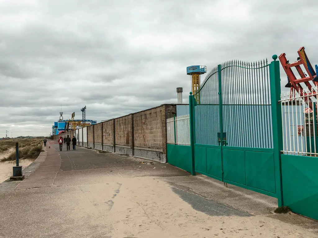 The promenade leading ahead, with a big wall and closed green gate on the right.