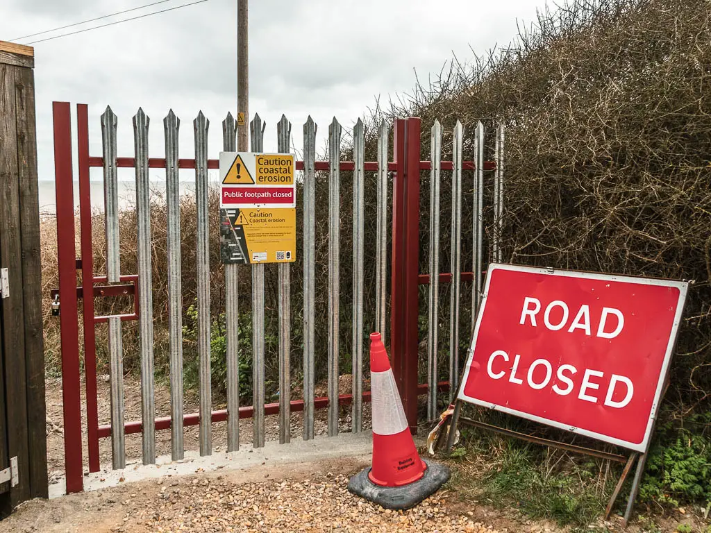 A metal gate blocking the path with a big red sign saying 'road closed'.