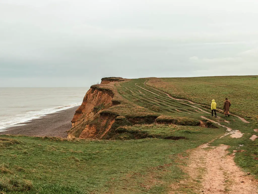 Two people walking along the trail on the clifftop, with the beach and North Sea below to the left.