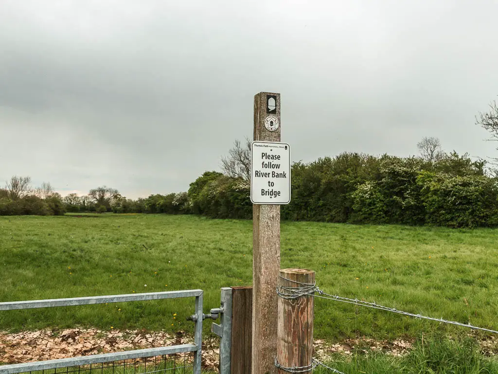 A wooden pole on a gate, with a white acorn sign on it, and big grass field on the other side.