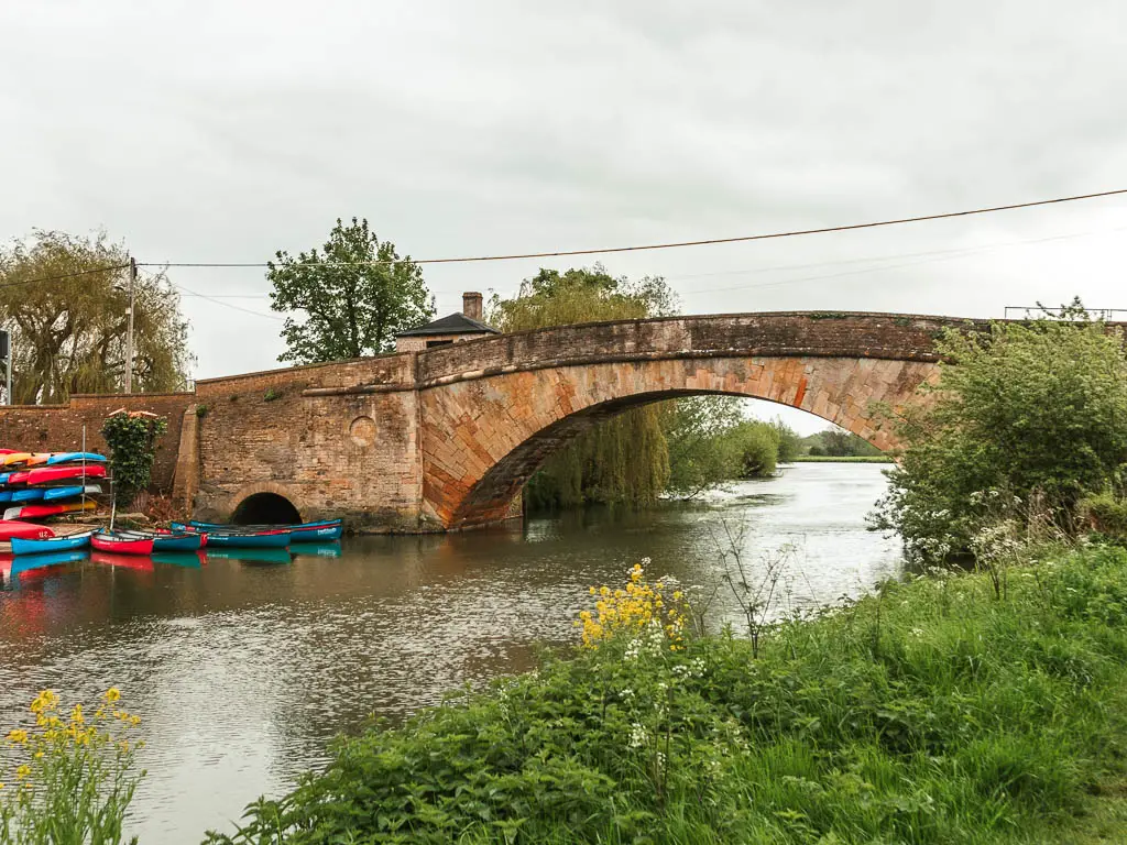 A stone arched bridge over the rover, with colourful canoes on the left in Lechlade.