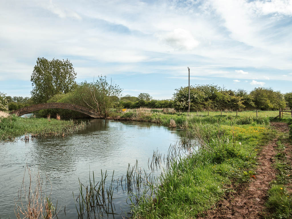 A dirt mud trail on the right, and river on the left, with a bridge ahead.