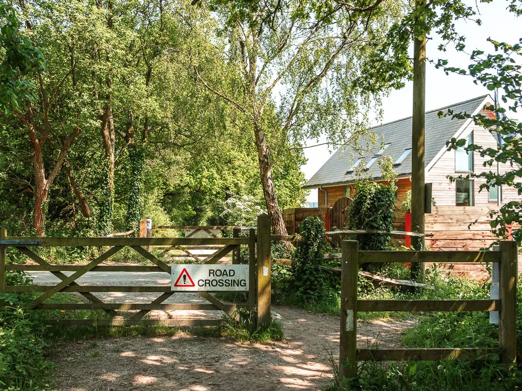 Wooden fences with a road and bustling on the other side. There is a sign saying 'road crossing'.