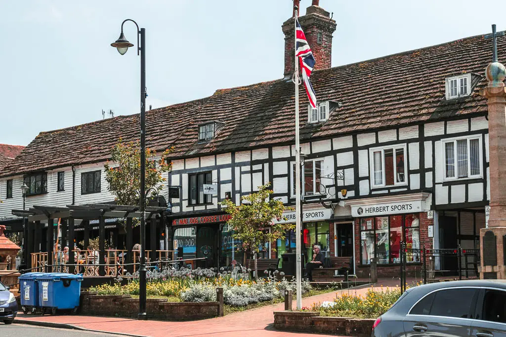 A row of Tudor building shops lining the street in East Grinstead. There is a tall white pole with the British flag flying on top.