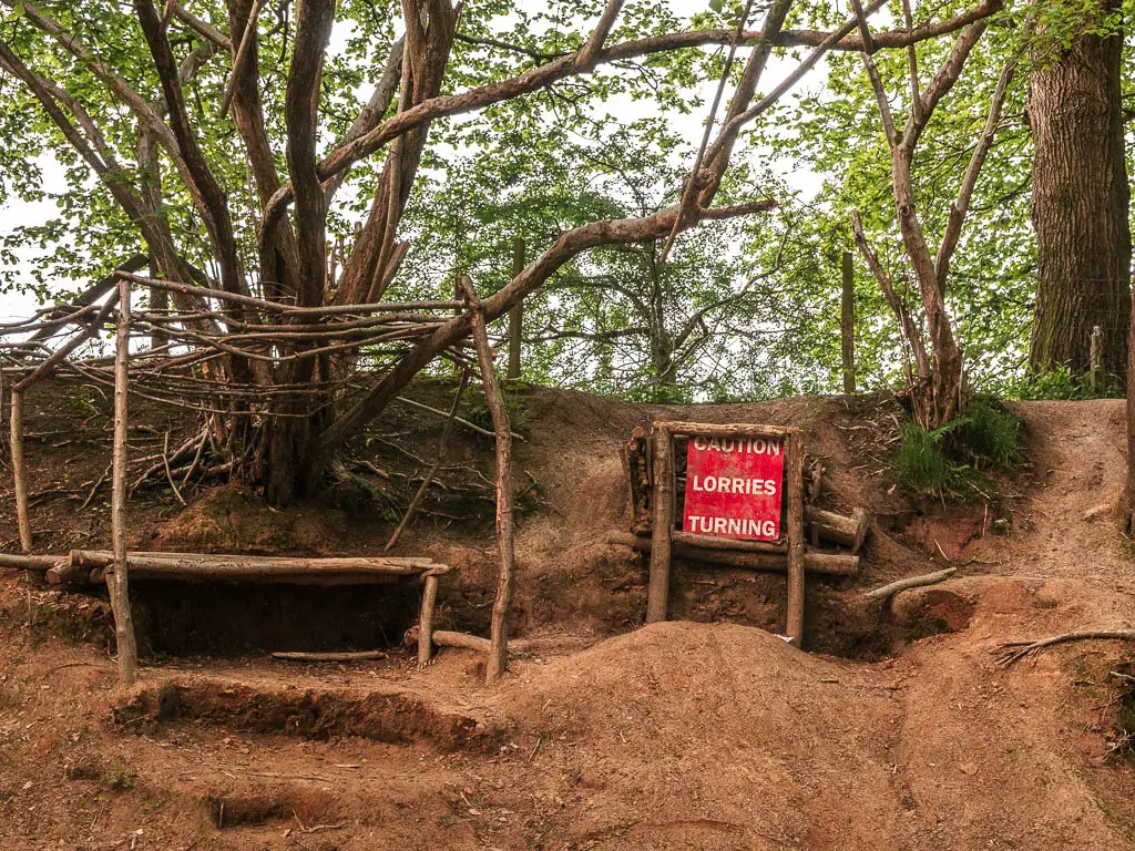 A rugged dirt bank, with thin tree trunks coming out of it and a red sign saying 'lorries turning'.