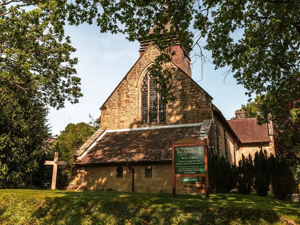 A church sitting on the grass. the frame of the photo is surrounded by overhanging leafy tree branches. 