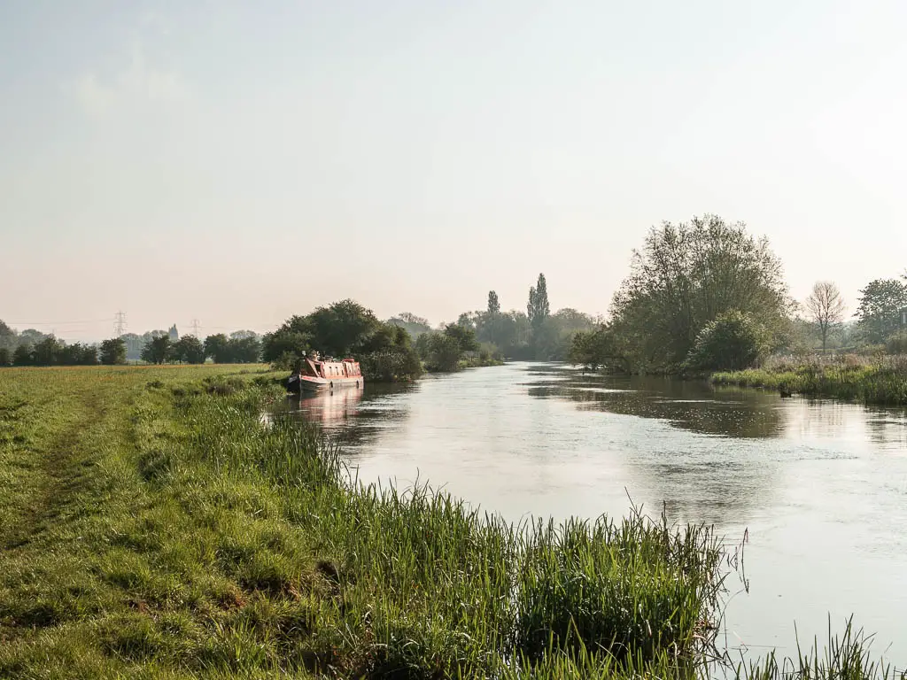 The river curving ahead on the right., and the green grass field on the left on the walk from Newbridge to Oxford. It's a misty day. There is a barge moored to the side ahead.