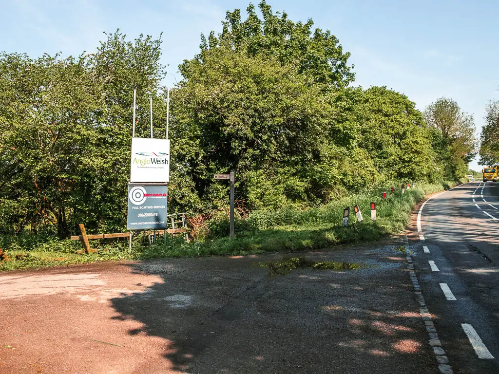 The right on the right leading ahead, and side road on the left. There are big information boards on the left side read, and green grass and bushes on the corner between the two roads.