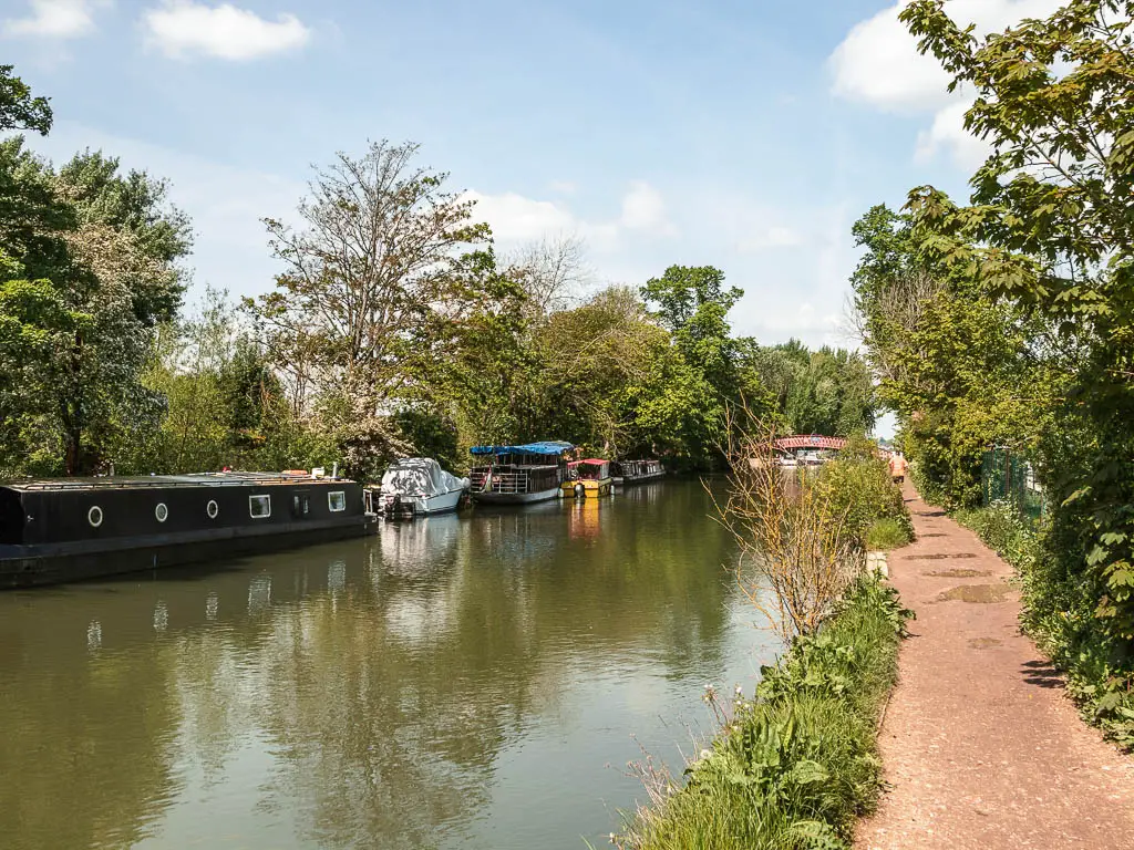 The river leading straight ahead, with a path on the right and barges and boats moored to the left side of the river on the walk into Oxford from Newbridge.