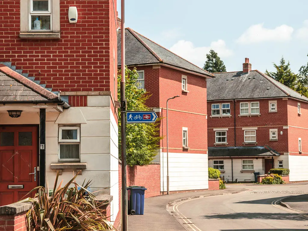 Red bricked houses in a residential area, with a pole and train station sign with a blue arrow pointing right.