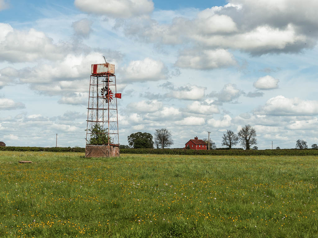 A large green grass field with a wind tower in the middle and a red bricked house on the other side.
