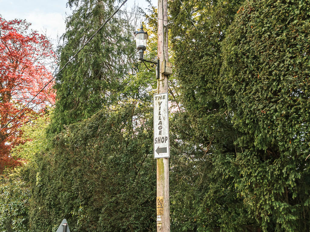 A white sign on a wooden pole saying 'the Village shop'.