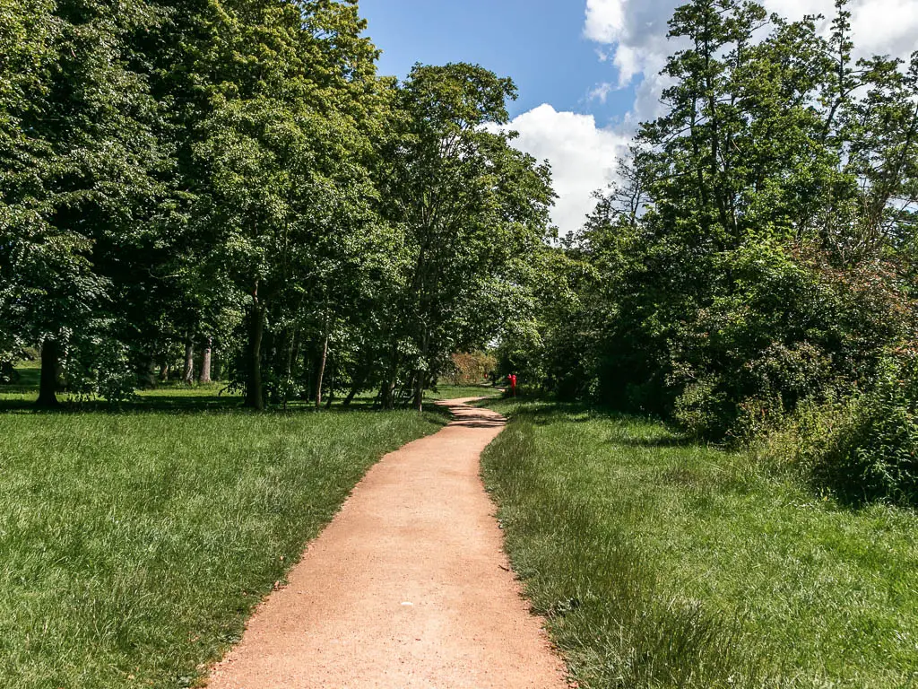 A wide path leading ahead through the grass field lined with trees ahead, near the start of the walk from Marlow to Maidenhead.