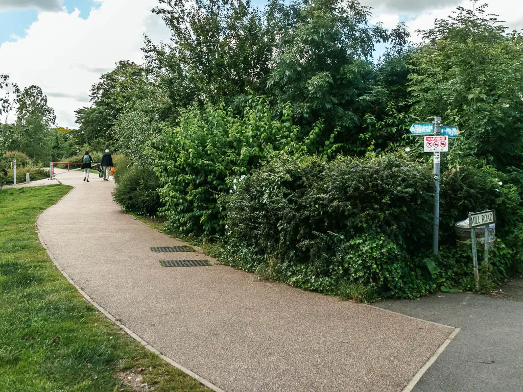 A path curving to the left, with neatly cut green grass on the left of it and green leafy bushes on the right.