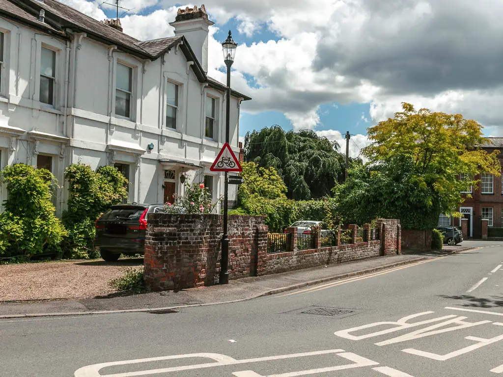 Looking across the road to a big white walled house in front of a brick wall on the other side.