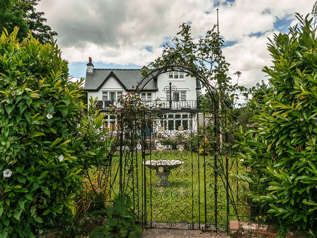 Looking through an ornate black metal gate to a neatly cute lawn and big white walled house, near the end of the walk from Marlow to Maidenhead.