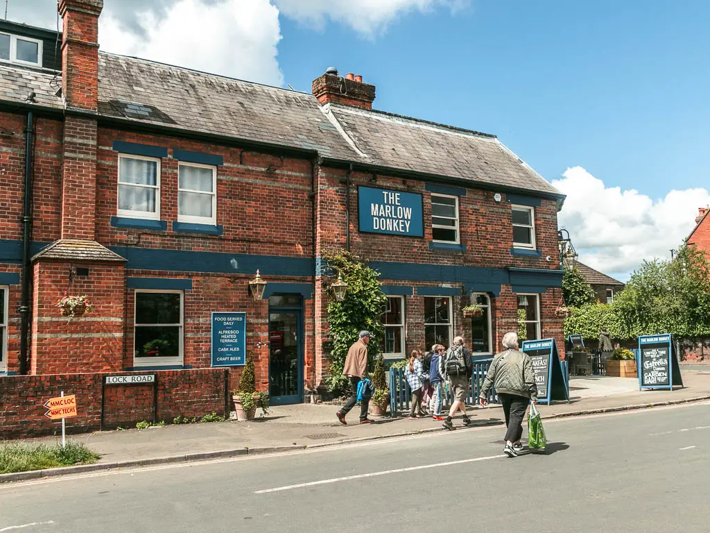 Looking across the road to the red bricked walled Marlow Donkey Pub. There are a few people walking next to it.