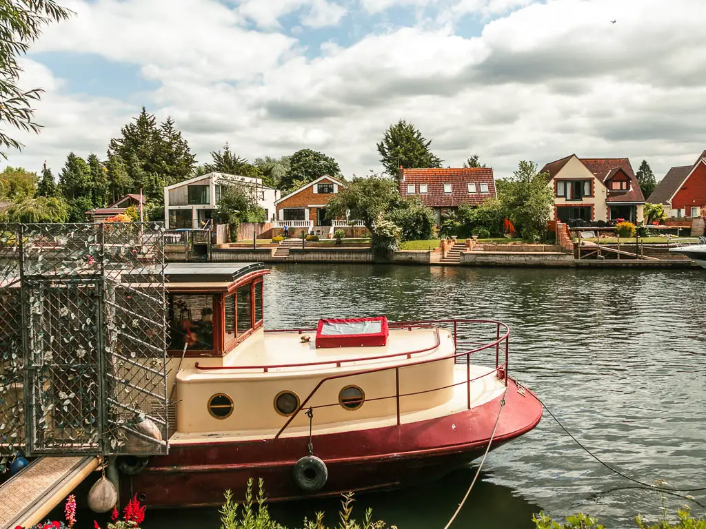 Looking across the river, with a cream and red boat moored to this side, and an assortment on houses on the other side, partway through the walk to Staines from Windsor.