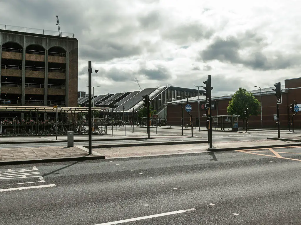Looking across the main road to a bike shed and sloped roofed building on the other side. Everything is grey.