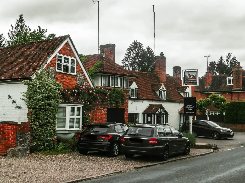 Looking across the road to a red bricked house and a white walled pub. There are a few cars parked outside.