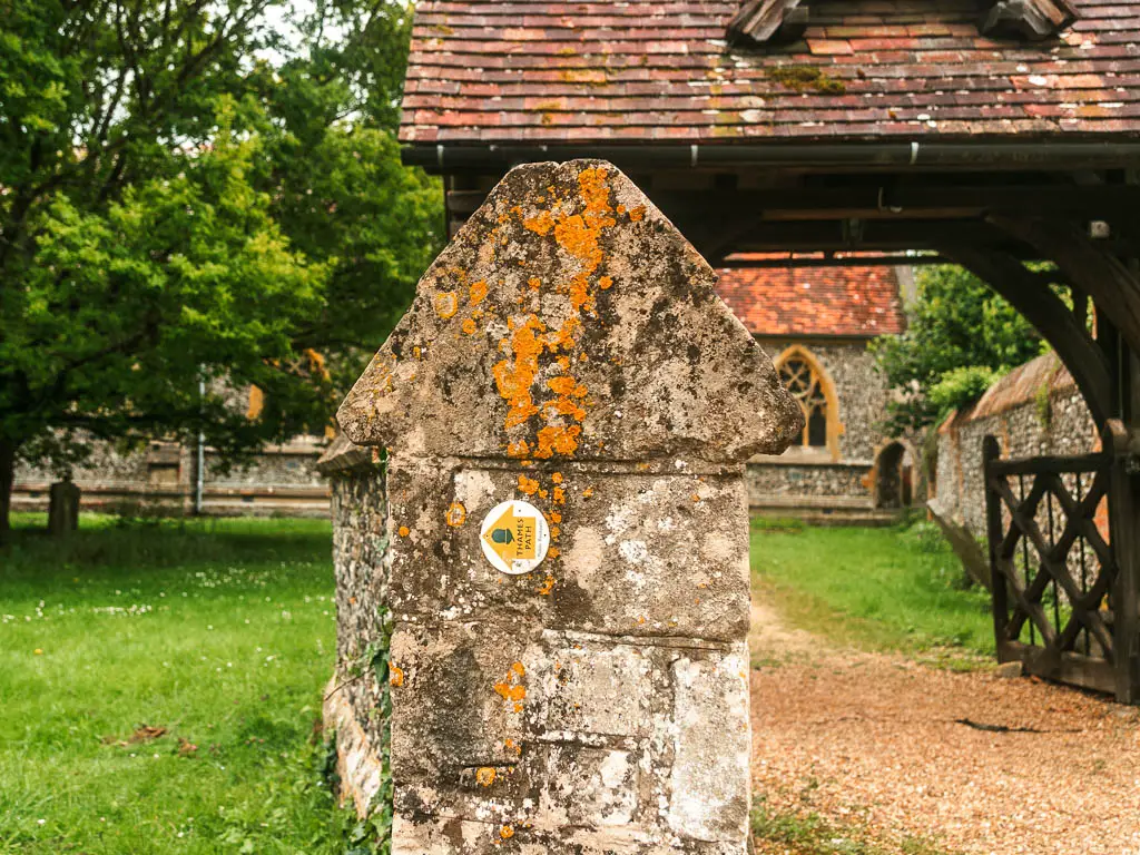 A yellow arrow on the end of a stone wall pointing left, with the church and green behind.