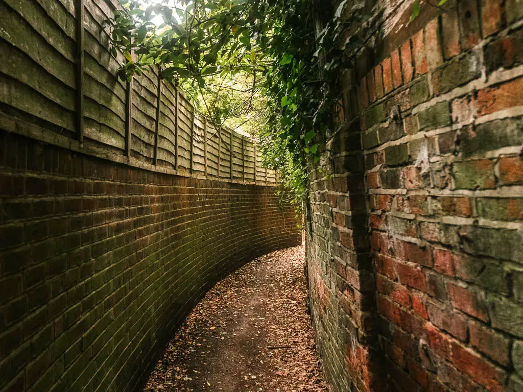 A path through an alley, lined with brick walls, curving to the right.