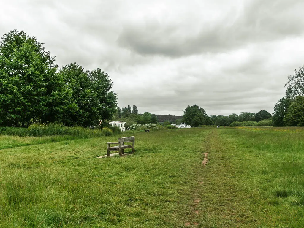 A large green grass field, with a bench in the middle facing to the left.