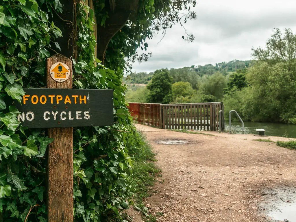 A footpath sign on wooden pole on the left in front of green ivy, and a walking path on the right in Goring and Streately.