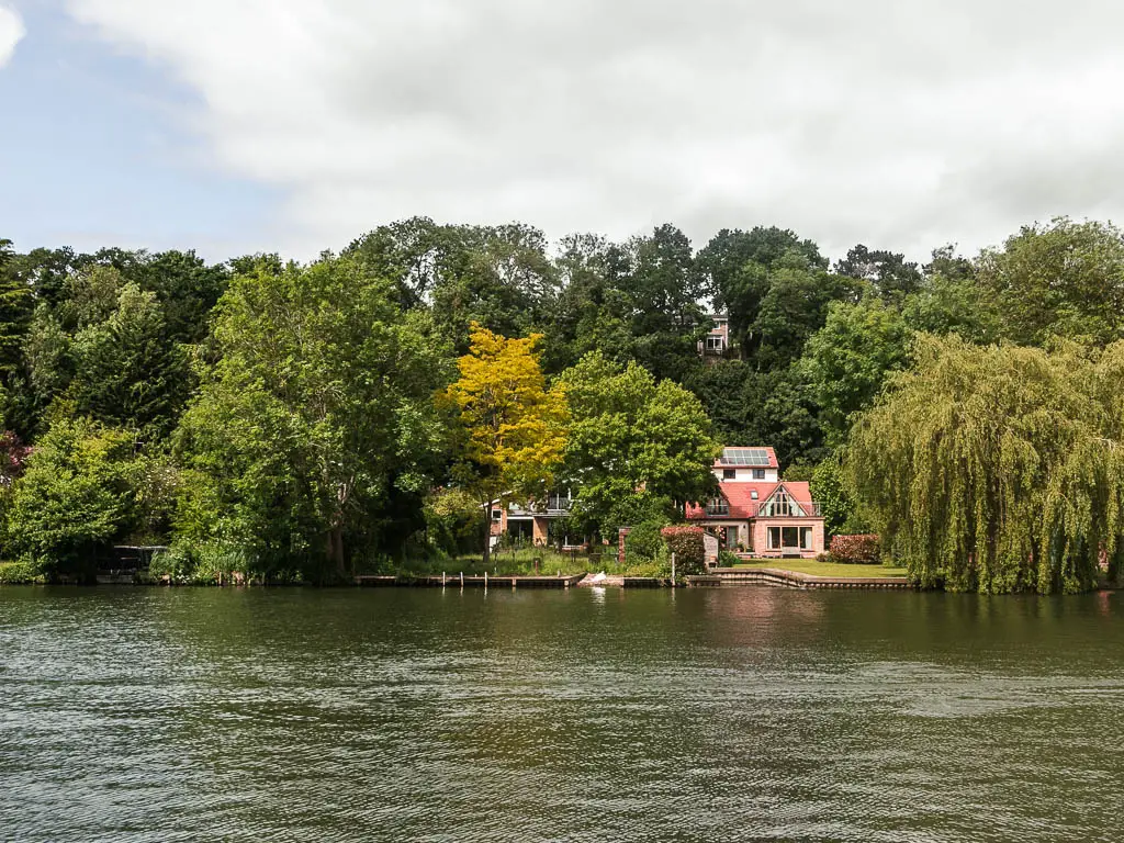 Looking across the rippled river to a mass of trees on the other side, and a partially hidden house.