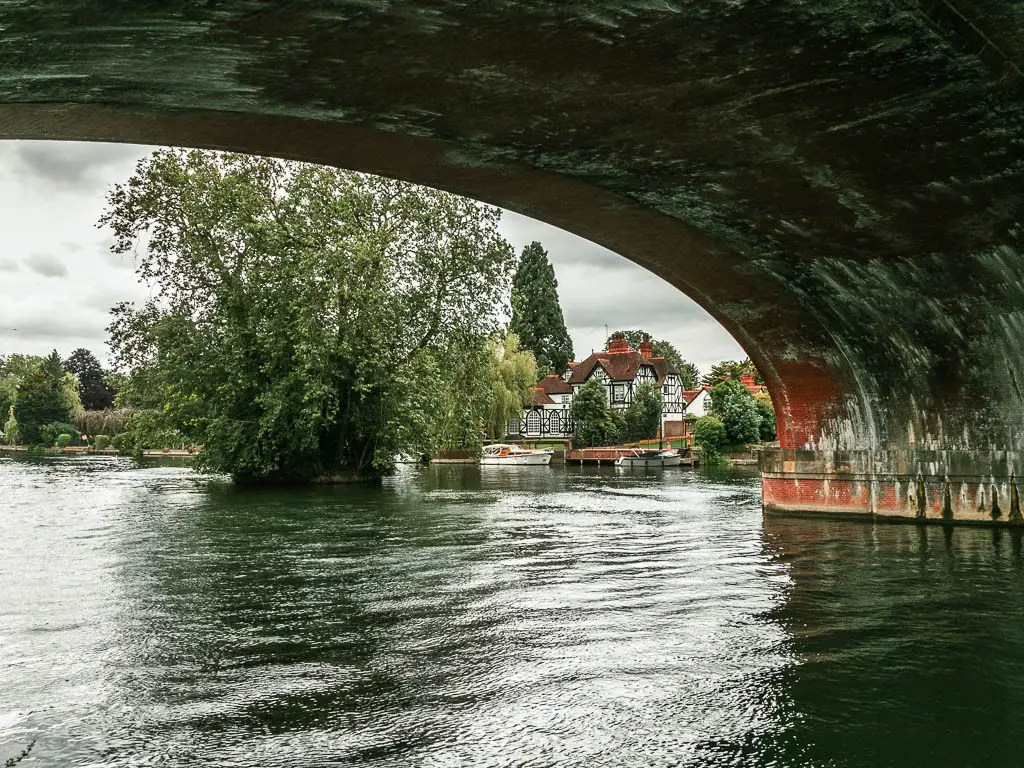 Looking under the curved bridge over the river, on the walk from Maidenhead to Windsor. There is a big Tudor house on the other side of the rive, and a big tree in the river next to it.