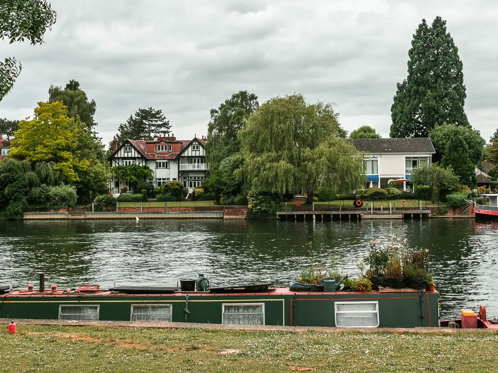 Looking over the green to the river, with a green barge moored to this side, and hoses and trees on the other side, when walking from Maidenhead to Windsor.