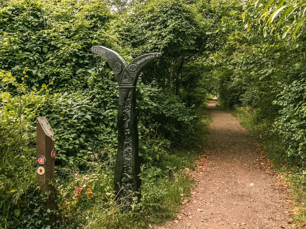 A dirt path leading ahead through the bushes and trees. There is a black sculpture on the left.