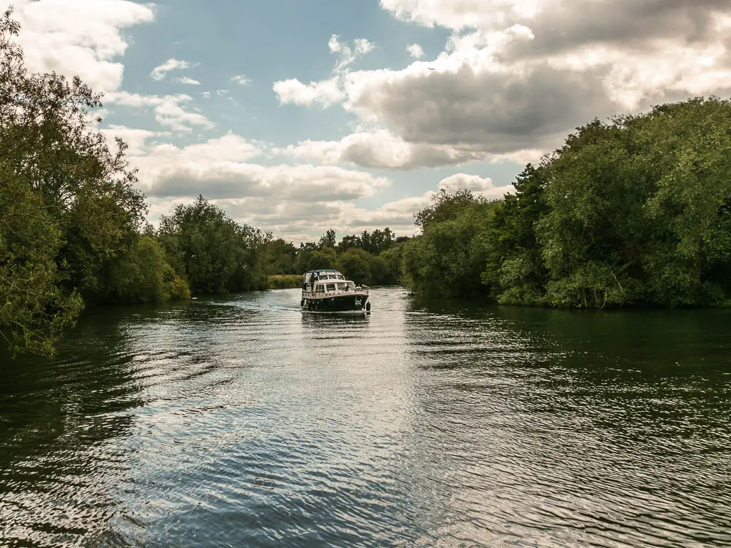 Looking along the wide river with ripples and big boat in the middle. There river is lined with masses of big green leafy trees.