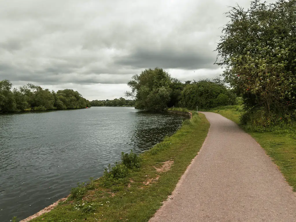 A walking path on the right, leading ahead and curving left. The river is to the left. There is a strip of grass between the two.