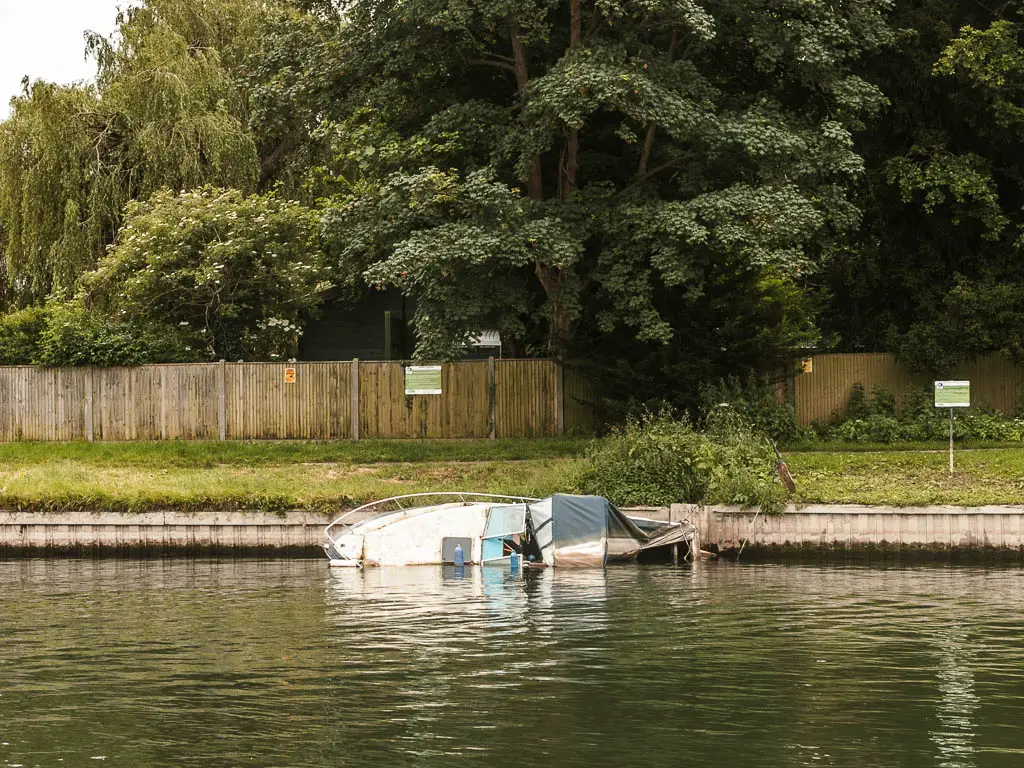 A boat half sunken on its side in the river.