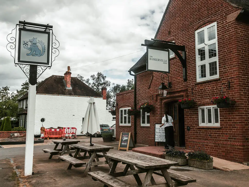 A brick walled pub, with wooden picnic benches outside.