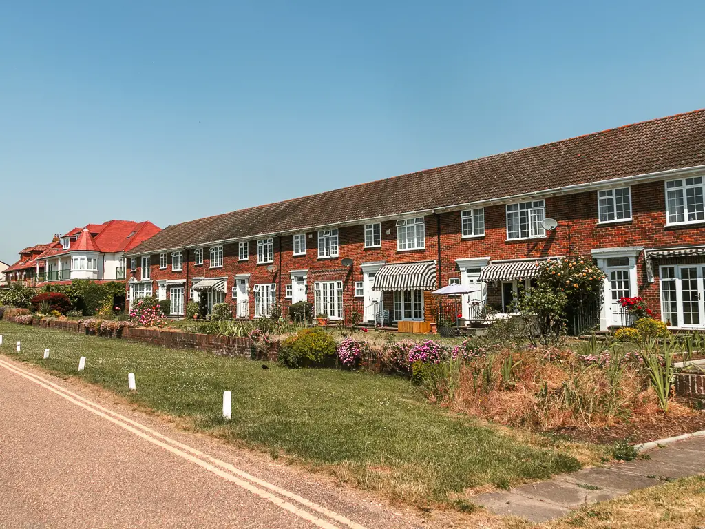 Looking at a row of terraced houses, with front lawn with flowers in front.