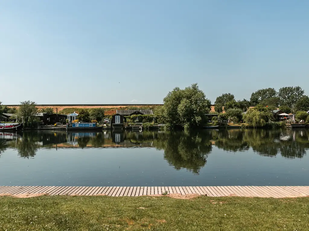 Looking across the green to the river with reflections from the trees and boats on the other side, on the walk from Staines to Shepperton.