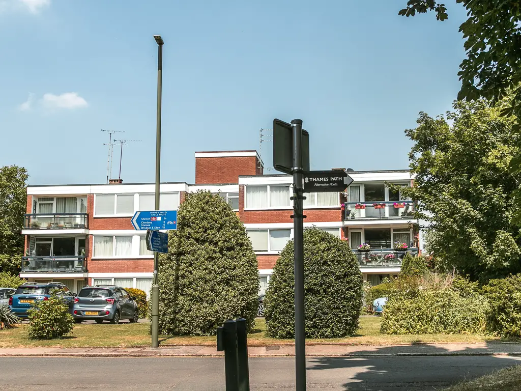 A road junction with a small apartment block on the other side. There is a thames path sign pointing right.