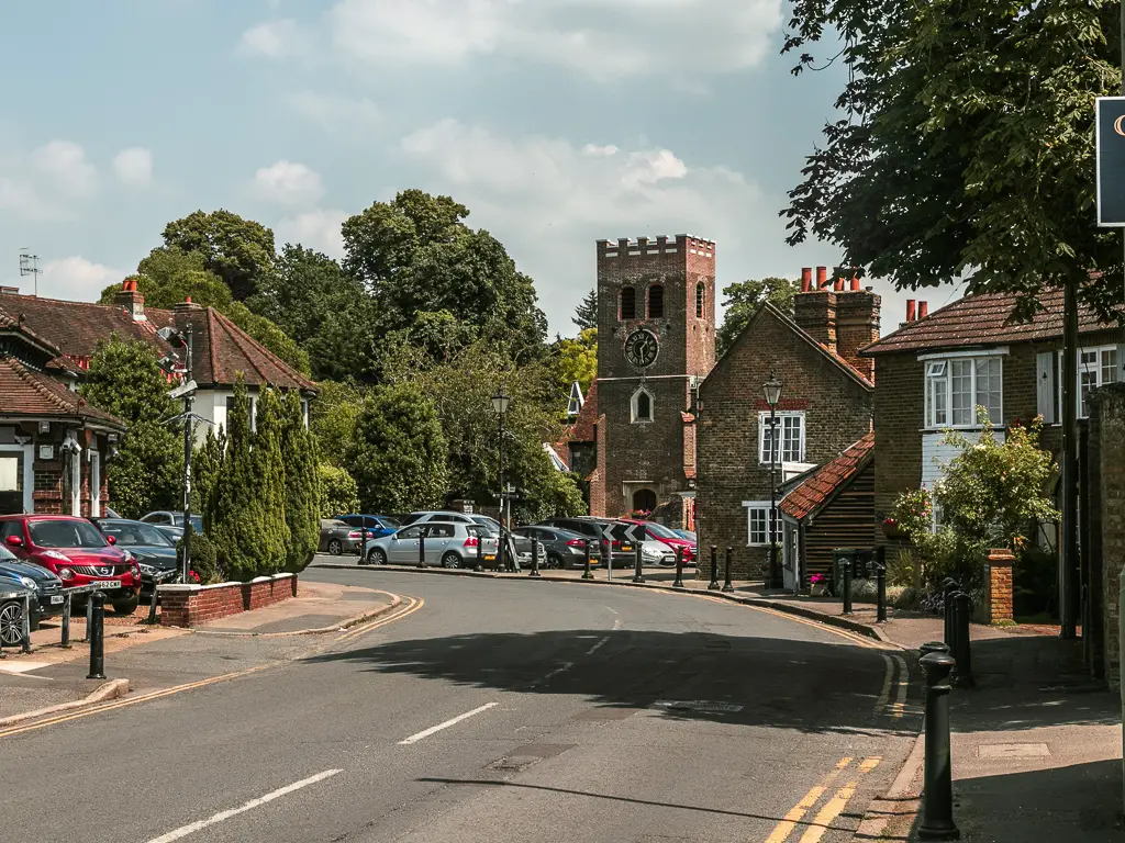 The road as it curves to the left with a church on the corner and cars parked below it.