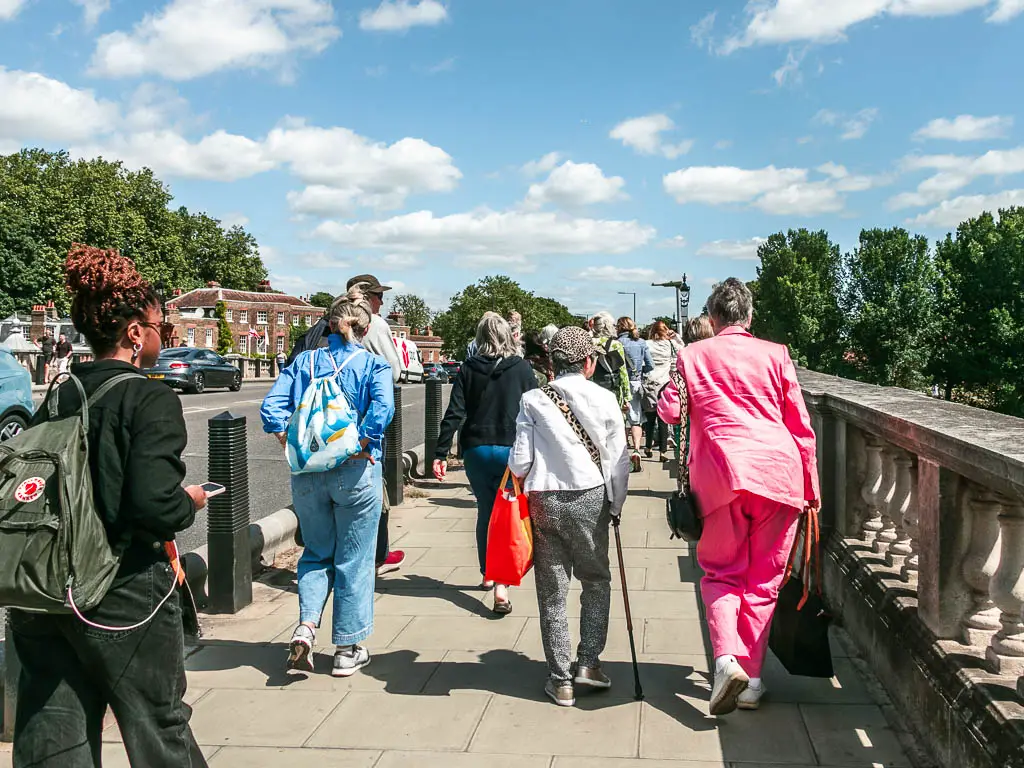 A mass of people walking along the pavement in Hampton Court with the road on the left.