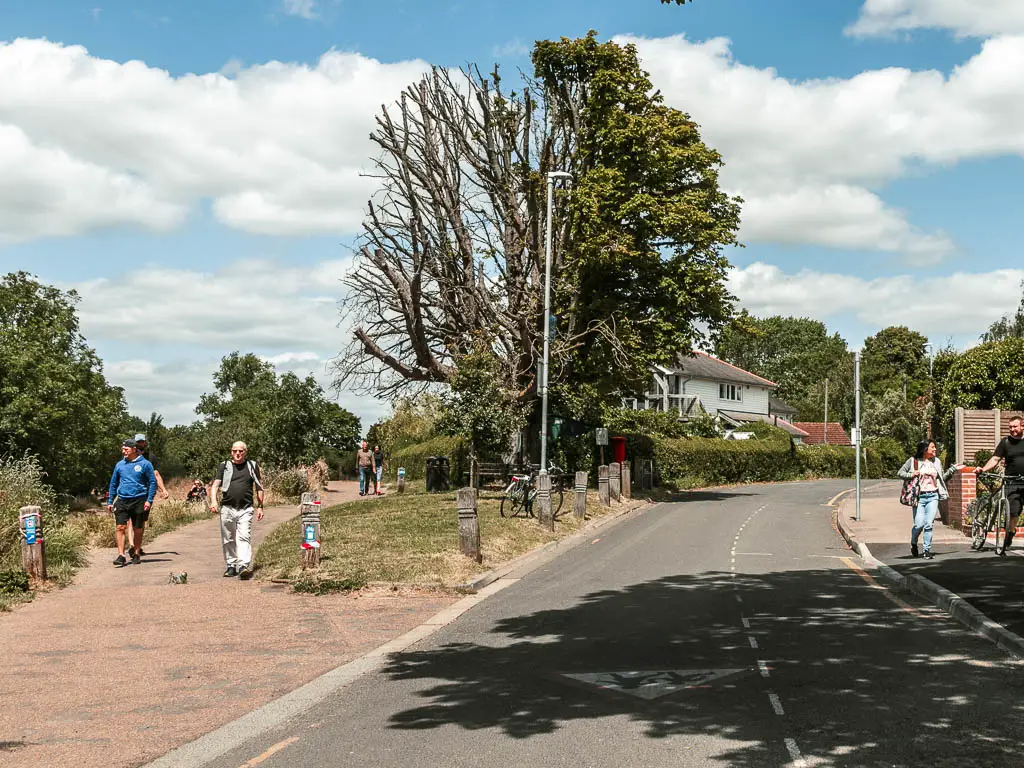 A road leading ahead to the right and a walking path coming off it to the left. There are people walking along the path.