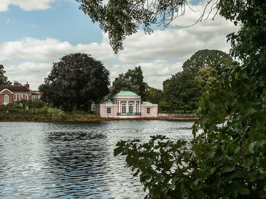 Looking across the rippled river to a pale pink buildings with light green sphere roof. There are green leaves coming into the Fram on the right.